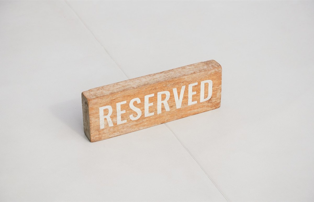 흰색 테이블 위에 놓인 나무 재질의 RESERVED 예약석 안내 표지